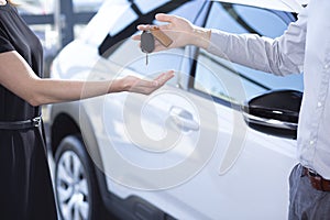 Close-up of seller`s hands with keys and buyer after transaction in car showroom