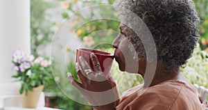 Close up of senior african american woman drinking coffee while sitting on the porch of the house