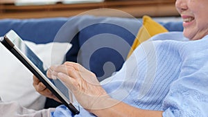 Close up of senior asian woman hand using digital tablet computer while sitting on sofa at home background, Happy retirement asian