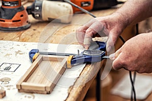 Close-up senior carpenter glueing wooden craft surface and joining with clamps. Woodwork carpenter with equipment and tools at