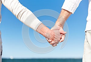 Close up of senior couple holding hands on beach