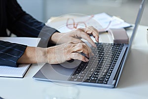 Close up of senior female hands typing at laptop keyboard working in office