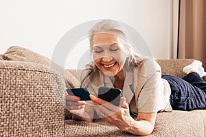 Close up of a senior female holding a credit card and smartphone. Adult smiling woman making a purchase with smartphone at home