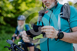 Close-up of senior man biker putting on bicycle gloves in nature.