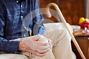 Close Up Of Senior Man Sitting On Sofa At Home Suffering With Knee Pain From Arthritis