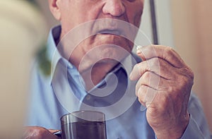 Close up of senior man taking medicine pill at home. Tinted photo