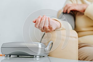 Close-up of senior sick woman checking her blood pressure and pulse indoors. Selective focus on tanometer, medical measuring