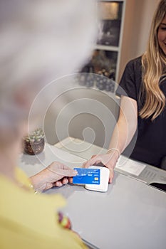 Close Up Of Senior Woman Making Contactless Payment To Stylist In Salon With Credit Card