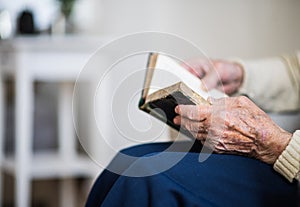 A close-up of senior woman reading Bible at home.