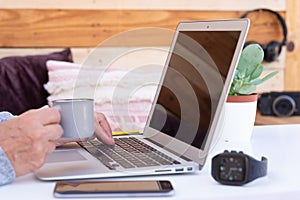 Close-up senior woman`s hands working on laptop outdoor on a white table drinking a coffee. Alternative outdoor office. Wooden