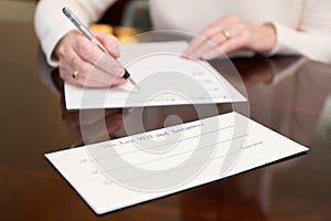 Close Up Of Senior Woman Signing Last Will And Testament At Home photo