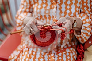 Close-up of senior woman sitting outdoor and knitting red scarf.