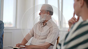 Close-up of serious senior adult male group leader speaking on teambuilding meeting. Business team sitting on chairs in