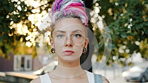 Close-up of serious woman with ear piercing, colorful hair and tattoo in park