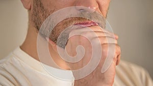 Close-up of serious young man with beard rubbing chin, having doubts, thinking