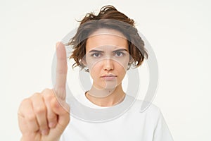 Close up of serious young woman shows one finger, stop, taboo gesture, disapprove something, blocking, saying one rule