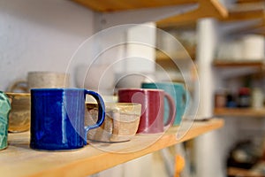 Close up of set of colorful handmade ceramic mugs on a wooden table inside a ceramic and pottery shop. Warm natural light