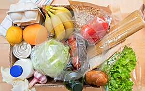 Close-up set of fresh packed food products in cardboard box on wooden table. Safe delivery. Food donation. Top view
