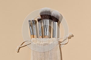 Close-up of a set of natural makeup brushes of different sizes in a storage bag on a beige plain background. The concept of makeup
