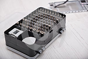 close-up of a set of screwdriver bits in a black box, gloves, a broken smartphone and a set of tools for replacing the glass of