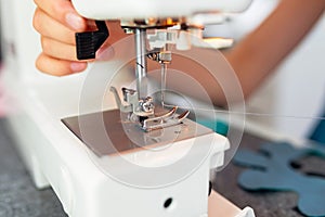 Close up of sewing machine and hand of seamstress at work. Child girl sews clothes on sewing machine