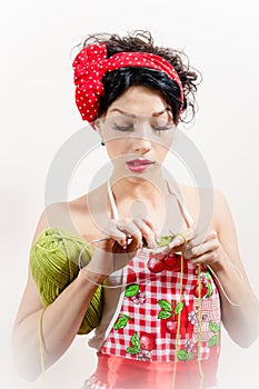 Close up on young brunette lady having fun wearing apron and red bow and doing knitting