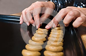 Female hands placing vanilla crescent roll cookies dough on black baking tray