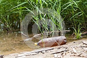 A close-up of shards of a plastic bottle against the background of water after people resting on the river bank. Garbage pollution