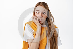 Close up of shocked and scared blond woman, biting fingers and gasping, staring startled and frightened, afraid of