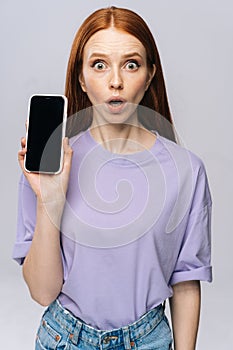 Close-up of shocked young woman in casual clothes holding cell phone with black empty mobile screen.