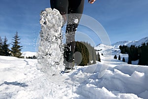 Close-up shoes of trail runner woman running in winter mountains trail on snow.
