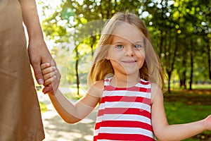 Close-up shoot of pretty small blond long-haired child girl in colorful dress holding trustingly hand of young mother