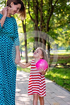 Close-up shoot of pretty small blond long-haired child girl in colorful dress holding trustingly hand of young mother