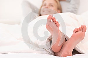 Close up shoot of woman`s feet relaxing in white bed in the morning