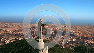 Close-up shooting from a drone on the sculpture of Jesus on mount Tibidabo and a view of Barcelona, the Mediterranean sea and