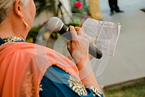 Close-up shot of an adult woman reading a speech with a microphone at a traditional Indian wedding