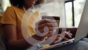 Close-up shot of an african american woman holding a credit card in her hand doing internet banking using laptop
