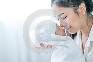 Close up shot of Asian mother kiss her newborn baby in front of white curtain in bedroom