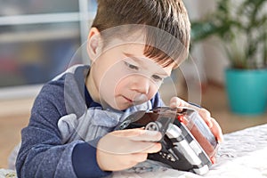 Close up shot of attractive brunet male kid plays with his favourite toy car, tries to repair wheel, has concentrated look, spends