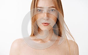 Close-up shot of attractive feminine naked redhead woman with freckles posing over gray background sensualy with