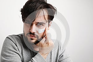 Close-up shot of attractive man with healthy skin, applies cream for anti wrinkle or anti aging, over white background.