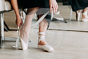 Close-up shot of a ballerina taking off the ballet shoes sitting on the floor in the studio