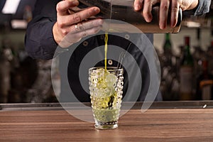 Close up shot of bartender hand pouring basil cocktail in a glass from shaker