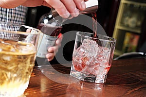 Close up shot of bartender hand pouring drink from measuring cup into a cocktail glass filled with ice cubes. Barman