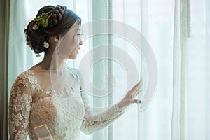 Asian bride standing near window in dressing room