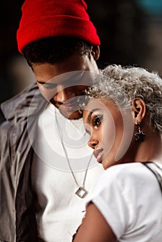 Close up shot of beautiful female mulatto with trendy hairdo and pensive look stands closely to her dark skinned male in