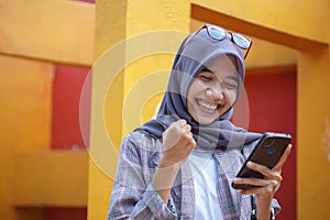 close up shot of beautiful muslim female student happy and holding smartphone in park