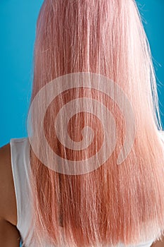 Close up shot of beautiful sleek natural long pink color dyed hair of young woman standing isolated over blue studio