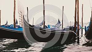 Close-up shot of beautiful traditional empty gondolas with rain covers rocking on waves at foggy pier in Venice, Italy.