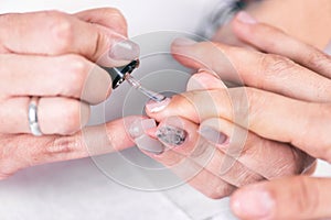 Close up shot of a beutician applying nail polish to female nail at nail salon.